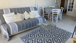 Una sala de estar con un sofá, una mesa de centro de vidrio, alfombra estampada y un comedor con sillas y una mesa.