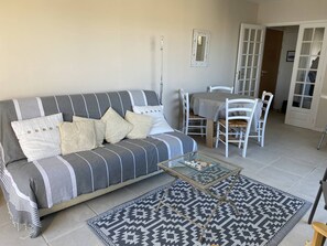 Un salon comprenant un canapé, une table basse en verre, un tapis à motifs et un coin repas avec des chaises et une table.