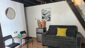 A compact living space with a sofa, a small table, two chairs, a refrigerator, and a decorative wall piece.