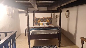 A four-poster bed with a 'HAPPY' sign, a small table, and a mirror on the wall.