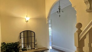 A hallway with a wooden floor, a bench with decorative items, a wall-mounted light fixture, and an arched doorway leading to another room.