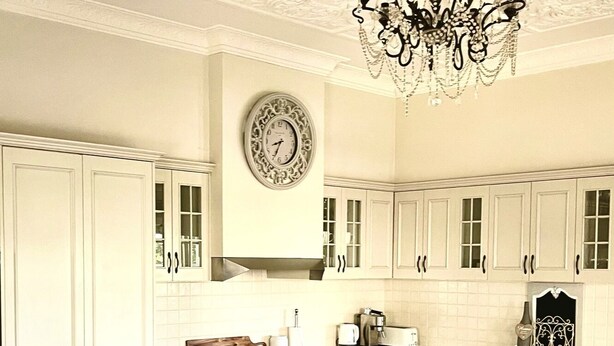 A spacious kitchen with white cabinetry, a central island, a chandelier, and a clock on the wall.