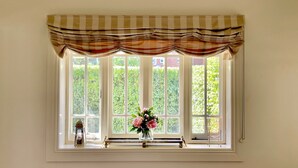A window with a checkered valance, a vase with flowers, and a small lantern on the windowsill.