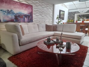 Un salon moderne avec un canapé d’angle blanc, une table basse en verre et un tapis rouge à longues mèches.