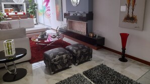 A modern living room with a fireplace, a dining area with a glass partition, and a large abstract painting on the wall.