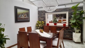 A dining area with a table, chairs, a chandelier, a framed picture, and potted plants.