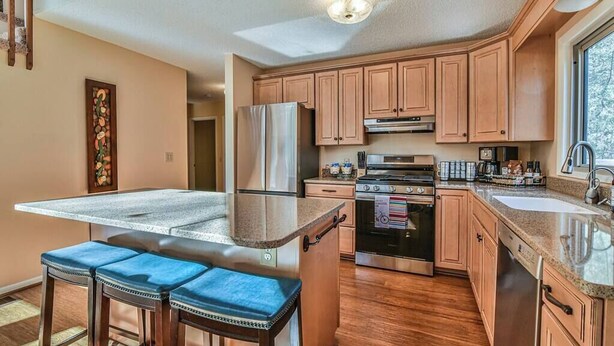A kitchen with wooden cabinets, stainless steel appliances, a granite countertop, and a bar stool.