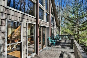 Una terraza de madera con mobiliario exterior, ventanas amplias y vistas al bosque circundante.
