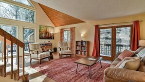 A spacious living room with a staircase, a fireplace, and a large window overlooking a snowy landscape.