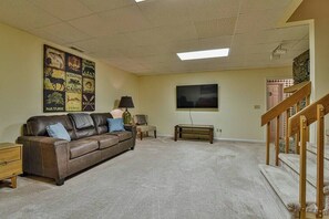 A living room with a brown leather couch, a flat-screen TV mounted on the wall, a lamp, and a staircase leading to an upper level.