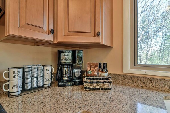 A kitchen counter with a coffee maker, a mug rack, and a basket of coffee beans.