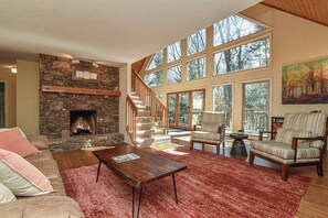 Ein großzügiges Wohnzimmer mit Kamin aus Stein, einer Treppe, großen Fenstern und einer gemütlichen Sitzecke.