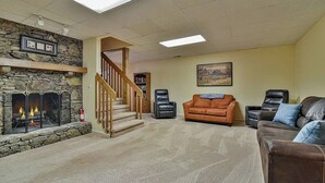 A living room with a stone fireplace, a staircase, and a large window.
