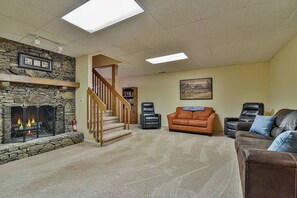 A living room with a stone fireplace, a wooden staircase, and a large window.