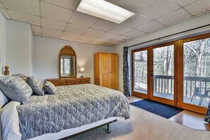 A bedroom with a large bed, a wooden cabinet, a mirror, and a sliding glass door leading to a deck.