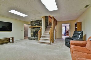A living room with a fireplace, a staircase, a black leather chair, and a large television.
