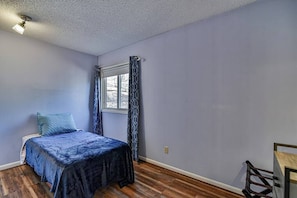 Un dormitorio con cama, ventana con cortinas y suelo de madera.