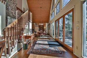 A spacious hallway with a wooden staircase, large windows, and a dining area with chairs and a table.