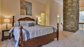 A bedroom with a large bed, a stone wall, and a painting on the wall.