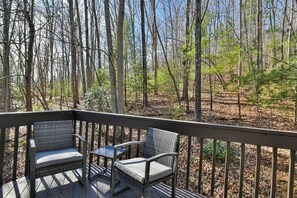A deck with wicker chairs and a small table, surrounded by a forest.