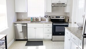 Una cocina moderna con armarios blancos, lavavajillas de acero inoxidable, horno negro y encimera de granito.