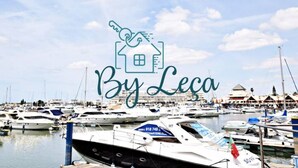 En lysthavn med mange både i havnen, et nøglesymbol over et hus, og teksten "By Leca".