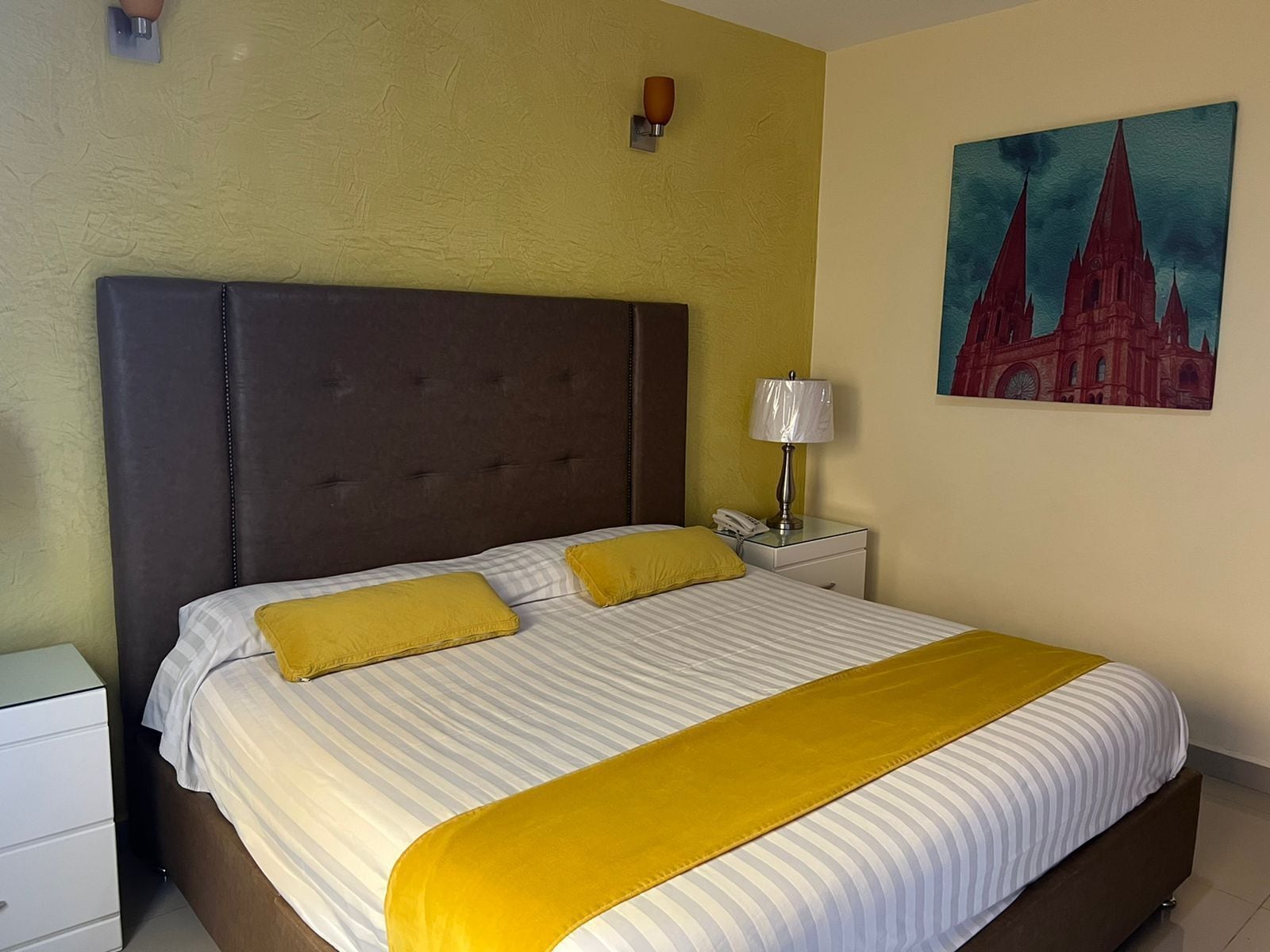 Et hotelværelse med en stor seng, et natbord med en lampe og et maleri på væggen.