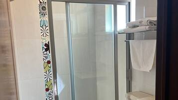 A bathroom with a glass shower enclosure, a toilet, and a sink with a towel hanging on the wall.