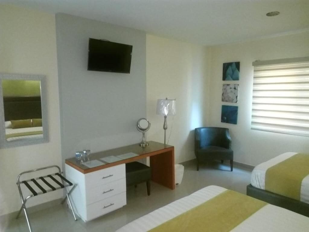Habitación de hotel con cama, escritorio con silla, televisor montado en la pared y obras de arte decorando la pared.