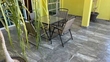 A dining area with a glass table and chairs, a potted plant, and a yellow wall.