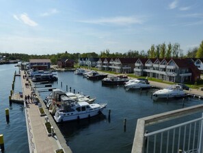 Uma marina com barcos atracados, um calçadão e casas em fila ao fundo.