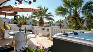 Terraza en la azotea con jacuzzi, mobiliario exterior y palmeras.