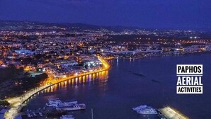 Vista aérea de una ciudad costera con un puerto deportivo, edificios iluminados y un muelle destacado.