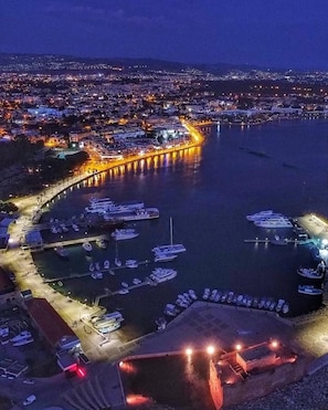 An aerial view of a coastal city with a marina, illuminated buildings, and a prominent pier. - Peyia Fontana - Executive spacious 2-bedroom apartment with Hot Tub & sea views (Peyia, Paphos)