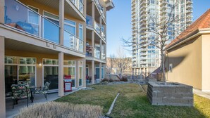 A modern apartment building with balconies, a small garden area, and a barbecue setup. - Garden level getaway at Discovery Bay (Kelowna)