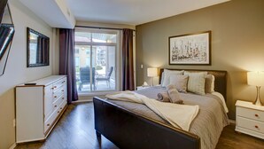 A bedroom with a bed, bedside tables, a dresser, a window with curtains, and a cityscape painting on the wall. - Garden level getaway at Discovery Bay (Kelowna)