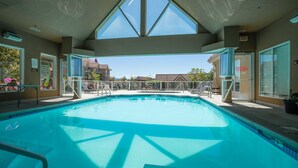 A swimming pool with clear blue water, surrounded by lounge chairs and a covered area with a view of buildings in the background. - Garden level getaway at Discovery Bay (Kelowna)