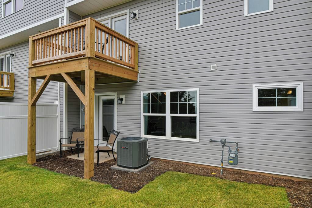 Une maison à deux étages dotée d’une terrasse en bois, d’un patio couvert et d’un grand climatiseur.