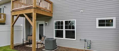 Une maison à deux étages dotée d’une terrasse en bois, d’un patio couvert et d’un grand climatiseur.