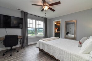 Ein Schlafzimmer mit Bett, Schreibtisch, Stuhl, Deckenventilator, Fernseher und einem Fenster mit Blick.
