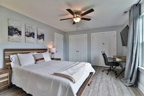 Ein Schlafzimmer mit einem Bett, einem Schreibtisch, einem Stuhl, einem Deckenventilator und Kunstwerken an der Wand.