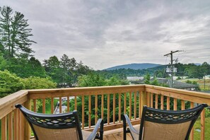 Eine Holzterrasse mit zwei Stühlen, die auf einen schönen Blick über ein bewaldetes Gebiet und eine entfernte Straße ausgerichtet ist.