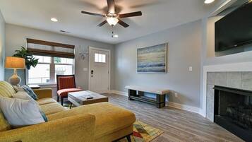 A living room with a sofa, a coffee table, a fireplace, and a ceiling fan.