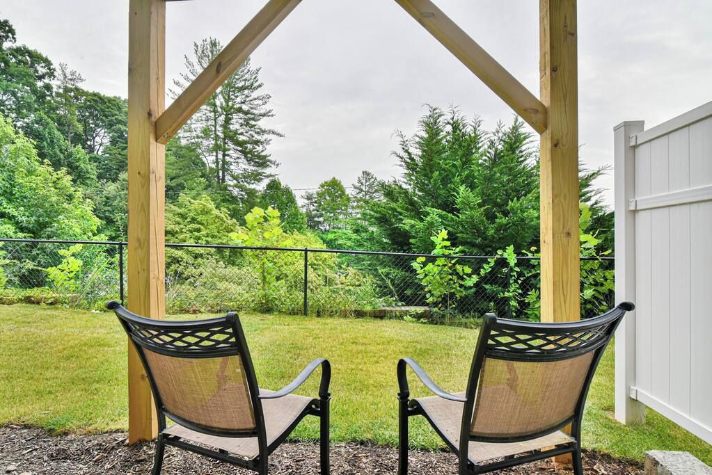 Zwei Stühle unter einer Holzw pergola mit Blick auf einen Rasen und Bäume.