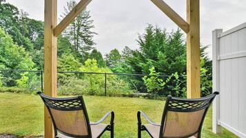 Zwei Stühle unter einer Holzw pergola mit Blick auf einen Rasen und Bäume.