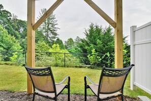 Dos sillas bajo una pérgola de madera con vista a un jardín césped y árboles.