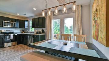 A modern kitchen with dark cabinets, stainless steel appliances, a wooden dining table, and a large window with curtains.