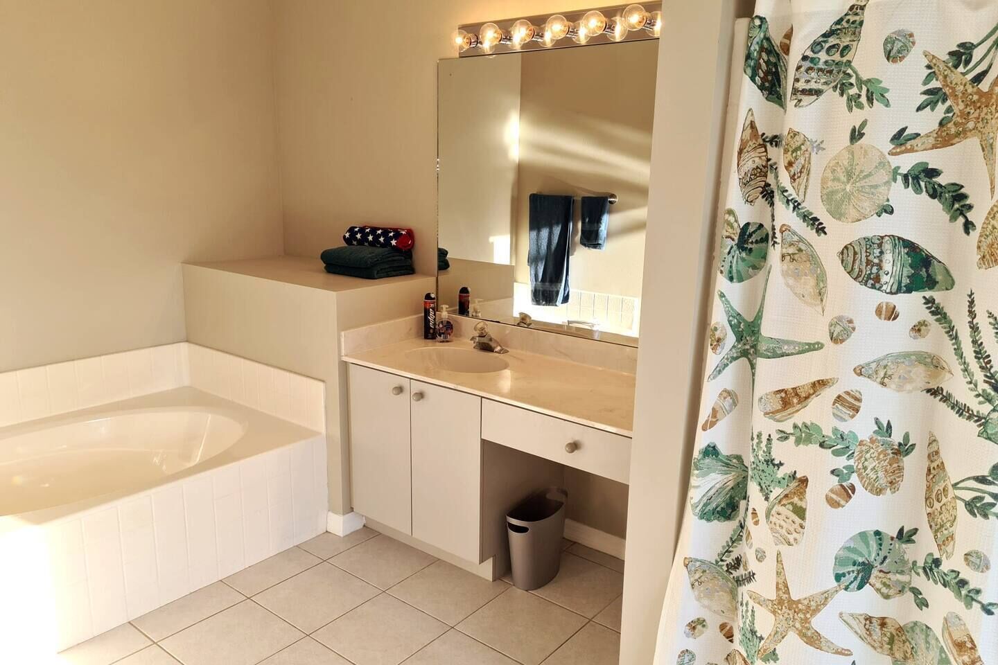 A bathroom with a bathtub, a sink, a mirror, and a shower curtain with a sea-themed pattern.