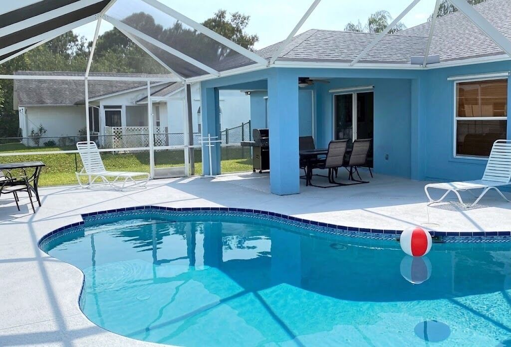 Una piscina con un patio coperto, poltrone prendisole e un barbecue.