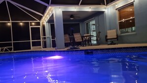 A swimming pool with a blue-lit edge, surrounded by a covered area with chairs and tables, and a view of the sky. - Screened Heated Pool, Boat Ramp Nearby, Beaches (Port St Lucie)